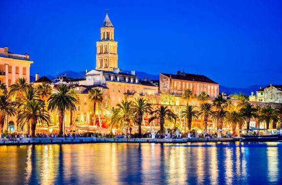 Split Riva by night, busy waterfront restaurants and bars, palm trees along the water and the cathedral lit up behind