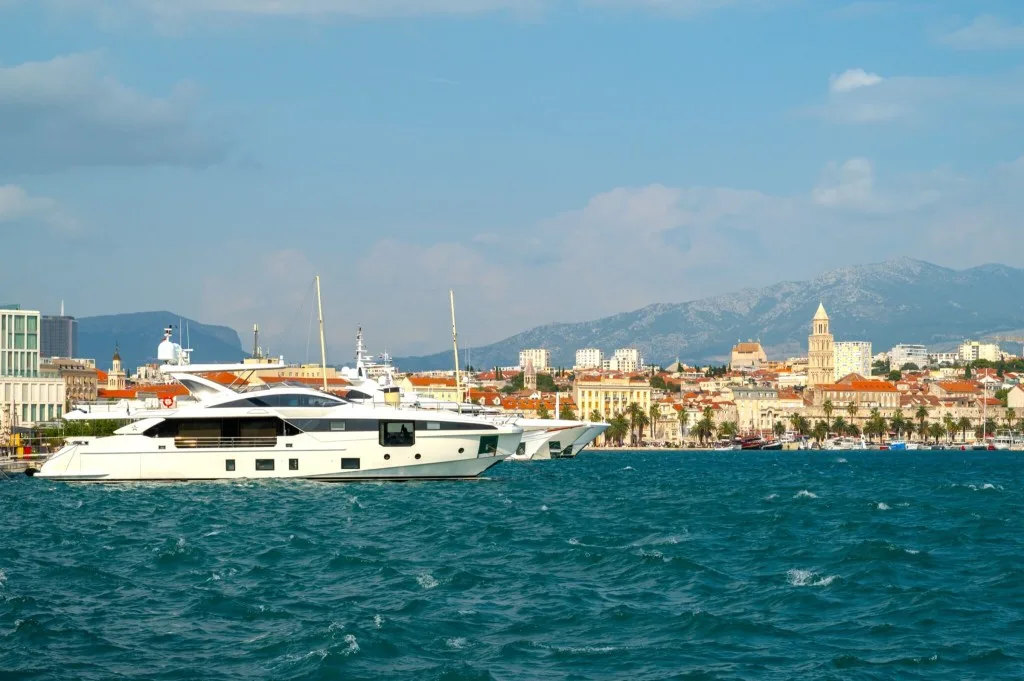 A large white motor yacht lying off the Split waterfront in Croatia, with the old town, the cathedral bell tower and the mountains behind