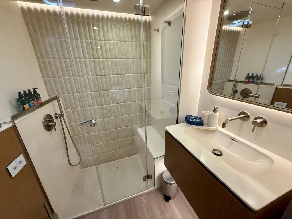 An en suite bathroom on catamaran MIDORI with a glass shower, light tiles and a wood vanity, September 2026.