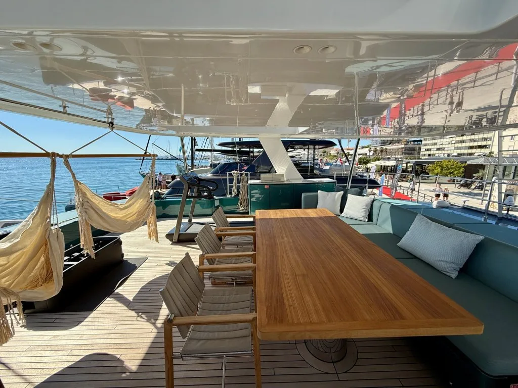 The flybridge of catamaran MIDORI with its long teak dining table, lounge and hanging chairs under the hardtop, September 2026.