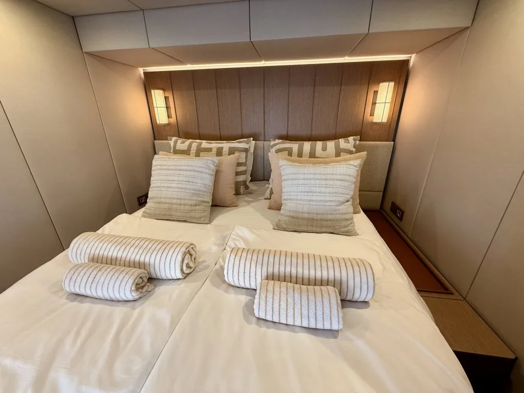 A guest cabin on catamaran MIDORI with a double bed that converts to twins, pale wood panelling and patterned cushions, September 2026.