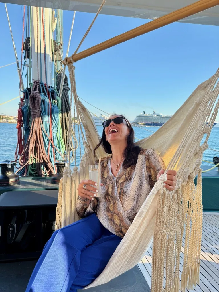 A DMA team member laughing in a hammock chair on the flybridge of catamaran MIDORI in evening light, Split, September 2026.