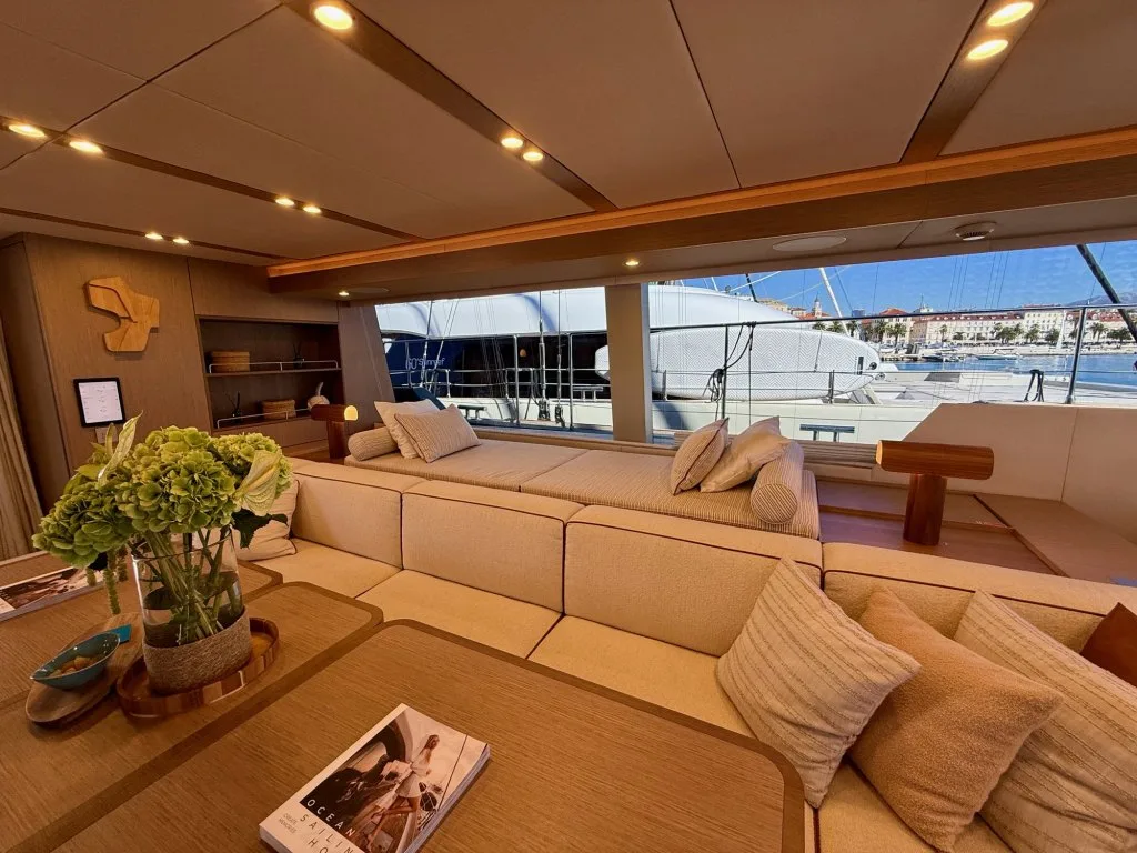 The lounge in the main saloon of catamaran MIDORI with a wraparound sofa and windows to the marina, September 2026.