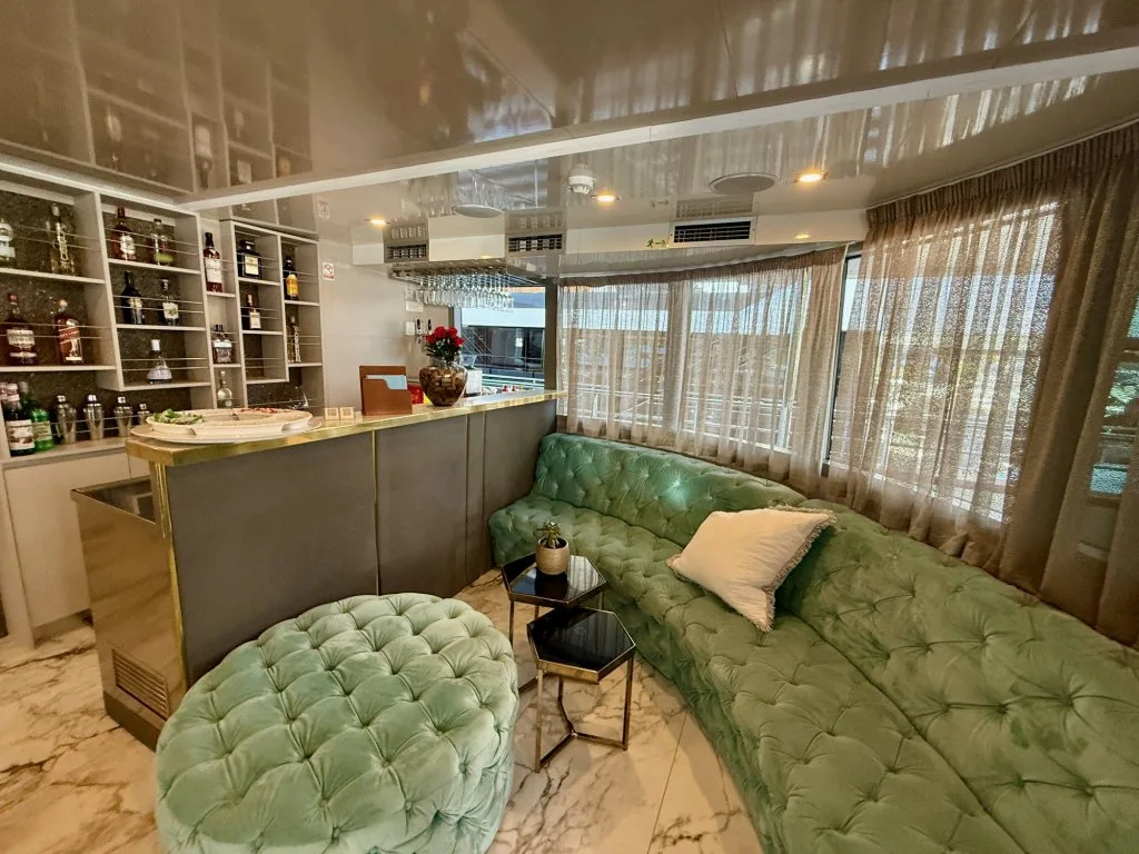 The bar lounge on motor yacht OHANA with a stocked back bar and curved green velvet sofas, September 2026.