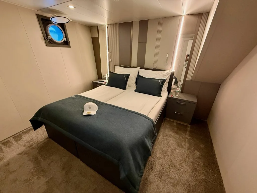 A double guest cabin on motor yacht OHANA with a porthole and dark blue bed runner, September 2026.
