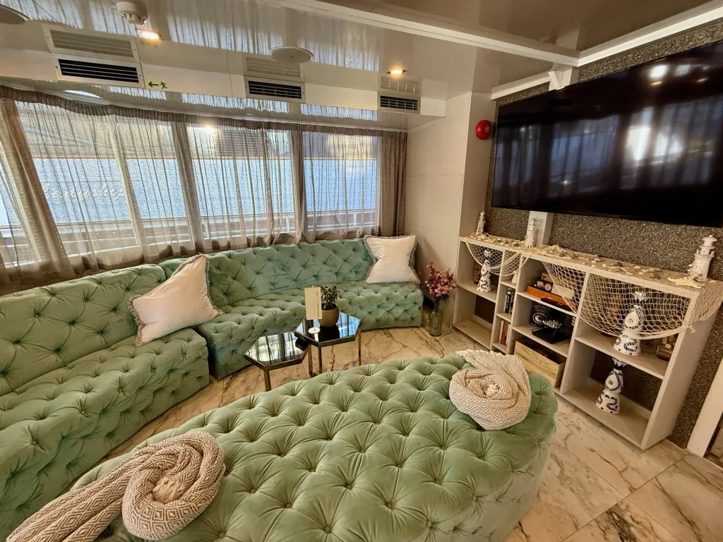 The lounge on motor yacht OHANA with green velvet seating and a large wall-mounted screen, September 2026.