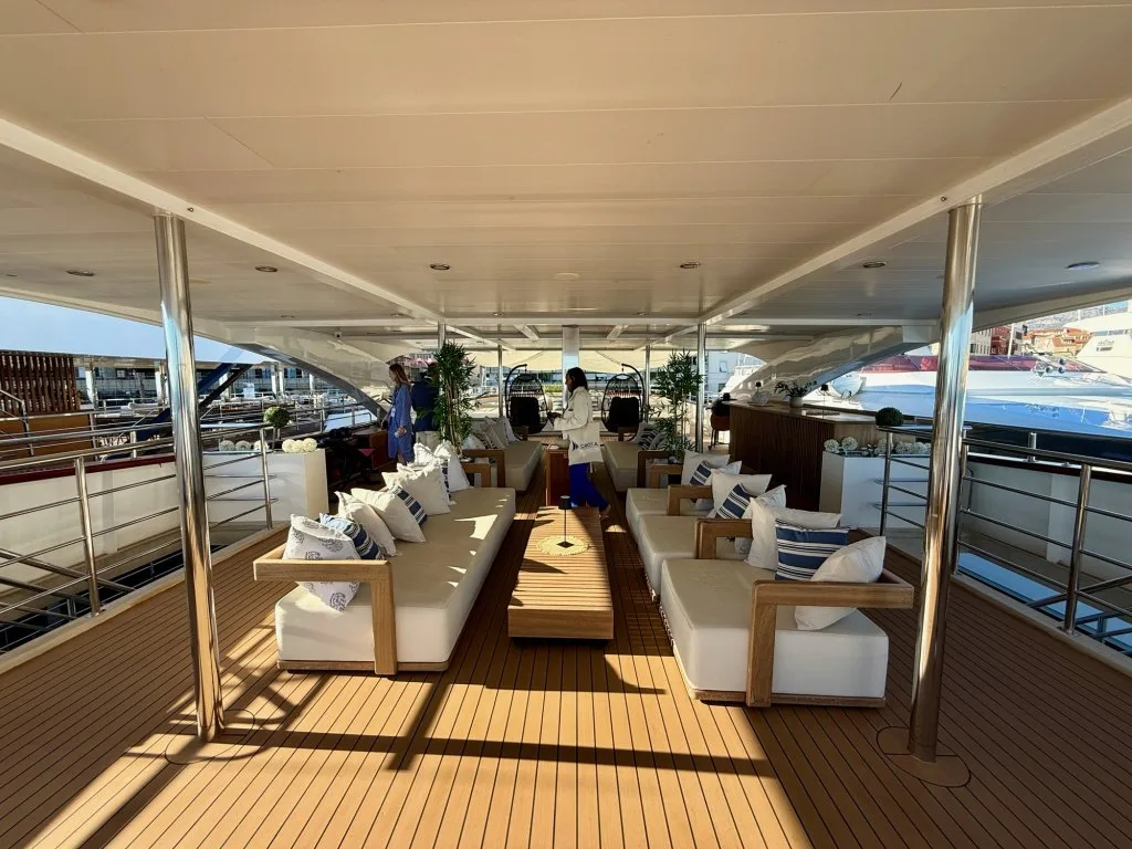 The shaded lounge on the sun deck of motor yacht OHANA with white sofas and tables, September 2026.