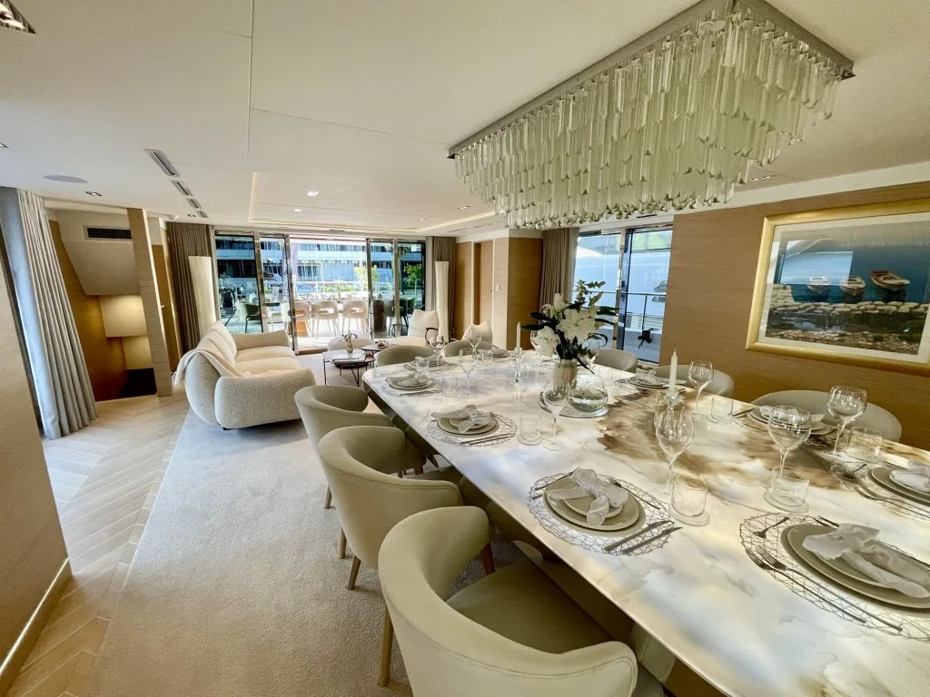 The formal dining table on motor yacht RENATA, a backlit stone top under a crystal chandelier, laid for dinner, September 2026.