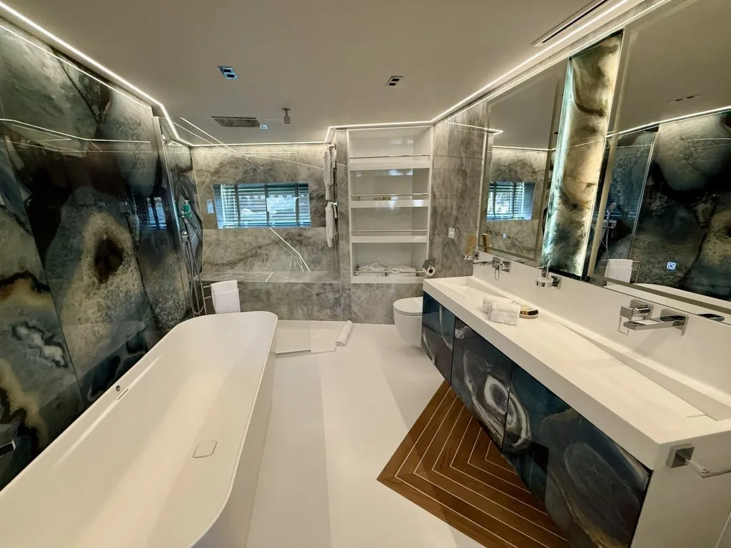 An en suite bathroom on motor yacht RENATA in dark marble with double sinks and a freestanding bath, September 2026.