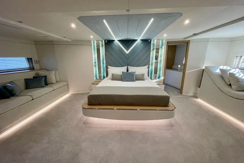 The master cabin on motor yacht RENATA, with the bed under a lit chevron headboard and a sofa beside it, September 2026.
