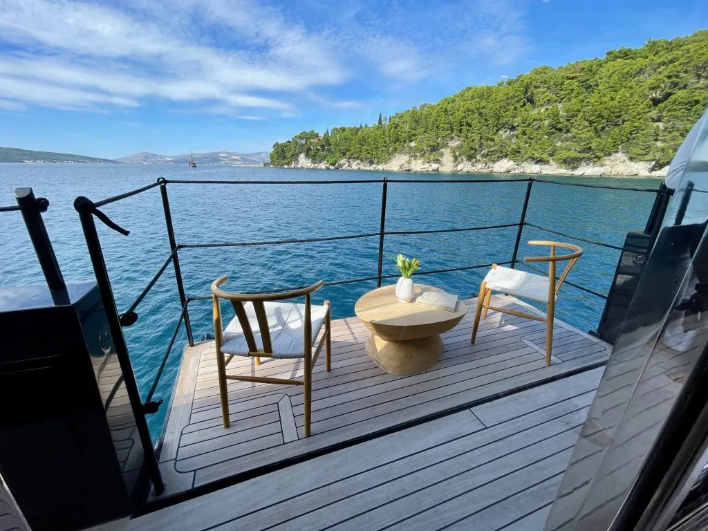 The fold-down side balcony on motorsailer REPOSADO with two chairs and a table over the water, coast behind, September 2025.