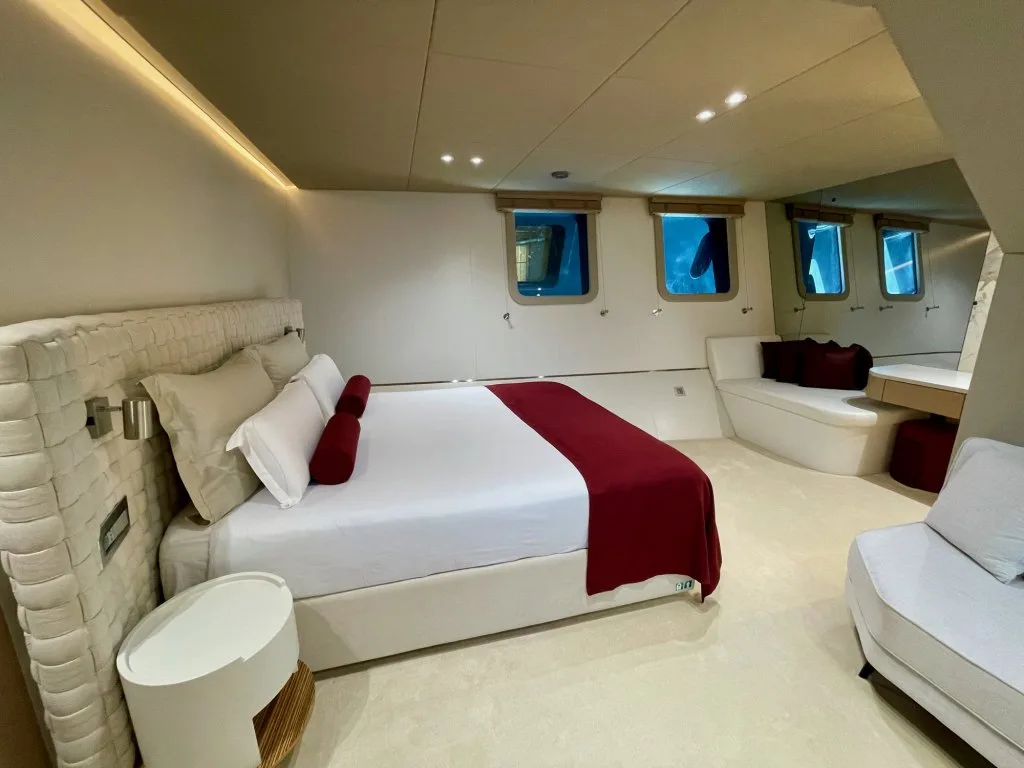 The master cabin of motorsailer REPOSADO with a wide bed, burgundy runner and seating, September 2025.