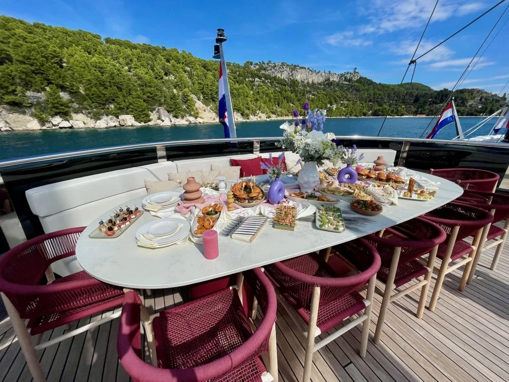 The sun deck table on motorsailer REPOSADO laid with platters, flowers and burgundy chairs, at anchor off Split, September 2025.