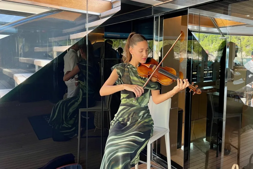 A violinist in a green dress playing in the saloon of motorsailer REPOSADO during the show lunch, September 2025.